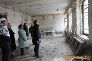 Группа людей в полуразрушенной комнате, предположительно бывшем Доме офицеров в Слониме, осматривает помещение с открытыми кирпичными стенами и разбитыми окнами.
