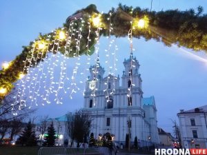Фарный костел Гродно на Новый год в сумерках, украшенный подвесными гирляндами и зеленью.